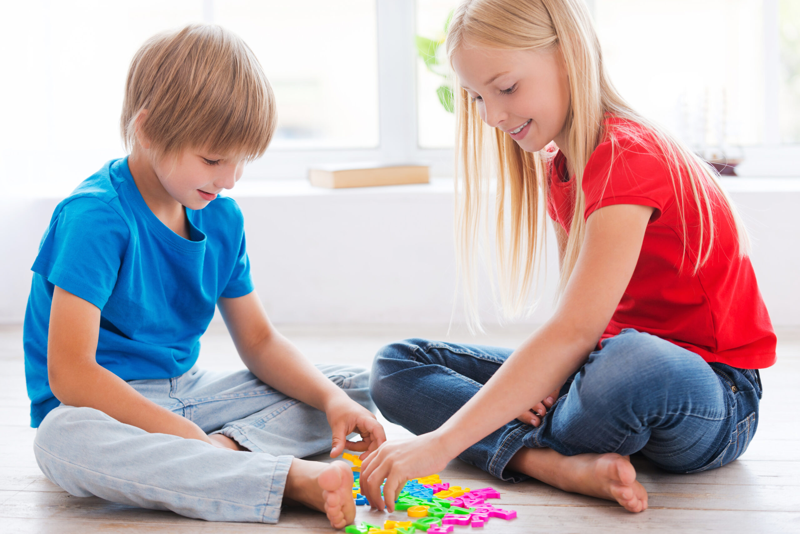 Kids playing at home. Two cute little children playing with plastic colorful letters while sitting on the hardwood floor