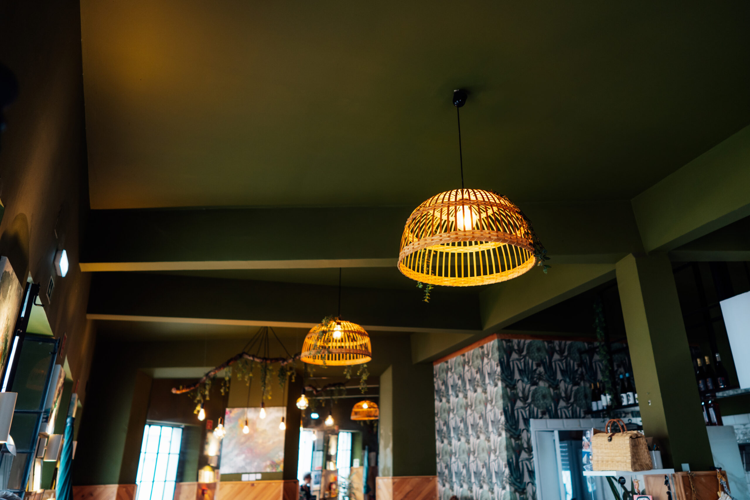 Wicker chandelier lamps on the dark green color ceiling in cozy cafe. Decorative bamboo ceiling lamps with clipping path, Hanging warm light wooden lamp. Eco natural trend. Modern interior design.